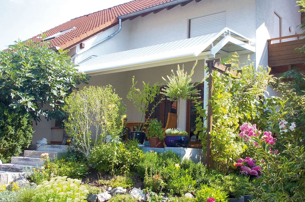 Terrassenüberdachung mit ausgefahrener Markise, davor ein bepflanzter Garten