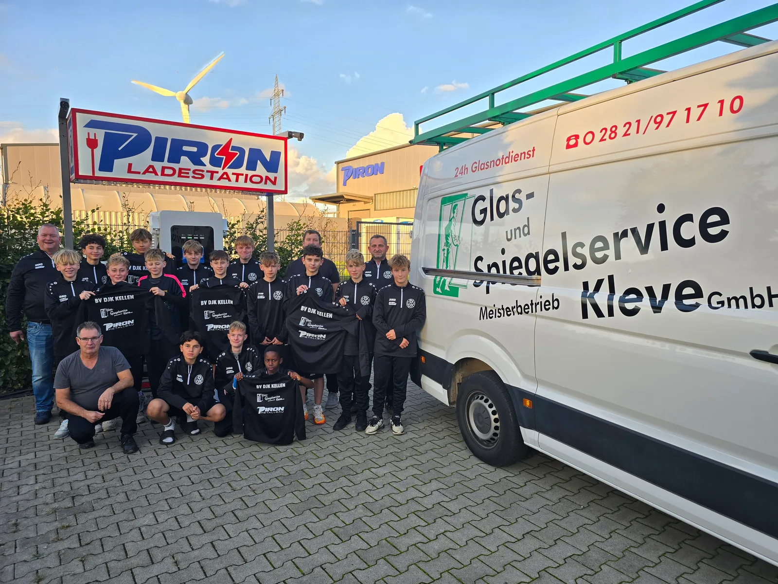 Die C2-Jugend des BV DJK Kellen mit Trainern und Betreuern vor der PIRON Ladestation in Kleve, daneben der Transporter von Glas- und Spiegelservice Kleve