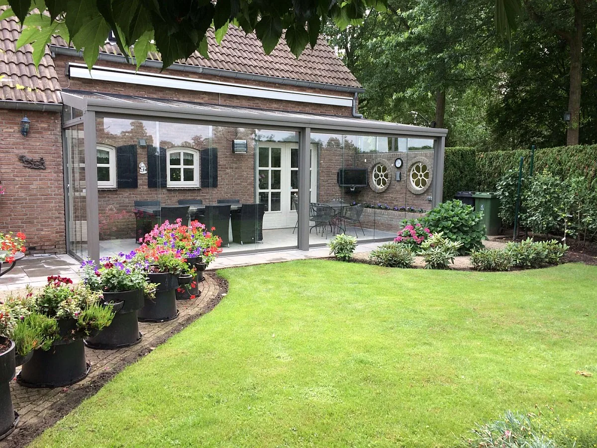 Terrassenüberdachung mit Glasdach an einem Backsteinhaus mit Garten