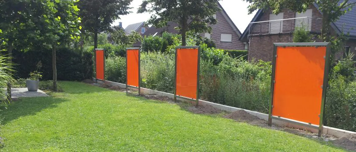 Sichtschutzzaun mit orangefarbenen Elementen in Metallrahmen im Garten