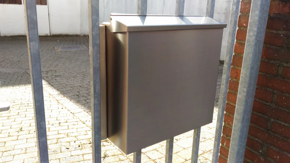 Briefkasten aus Edelstahl auf einem Standrohr vor einem Haus