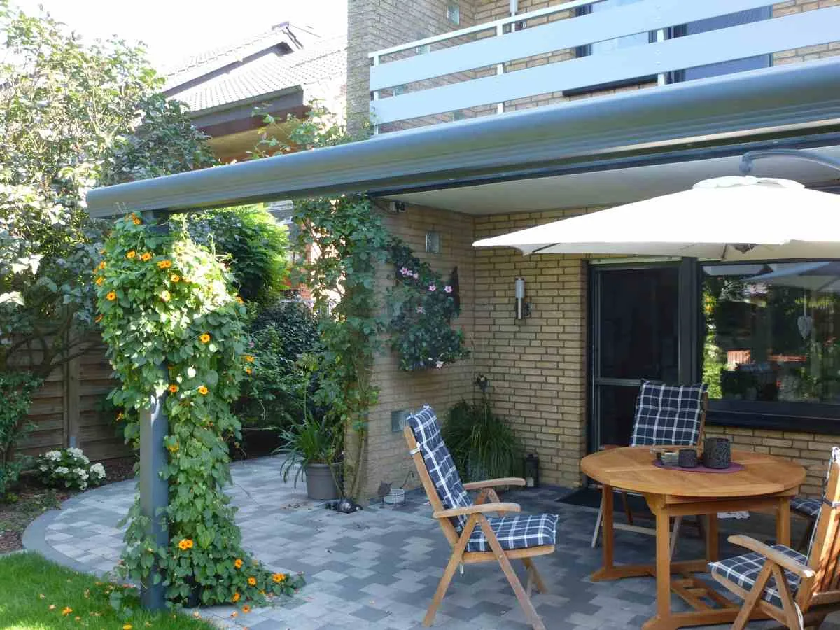 Terrassendach an einem Wohnhaus mit Balkon darüber, davor Gartenmöbel aus Holz und ein Sonnenschirm