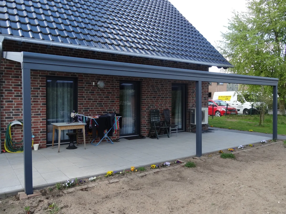 Breites Terrassendach an einem Neubau mit dunklem Dach, der Garten davor ist noch unbepflanzt